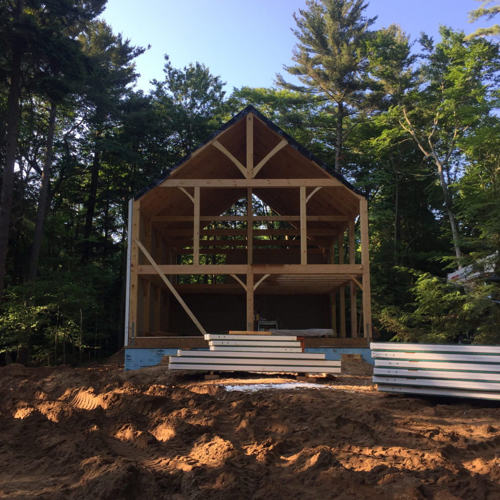 Front of the timber frame structure with a stack of SIPs in front